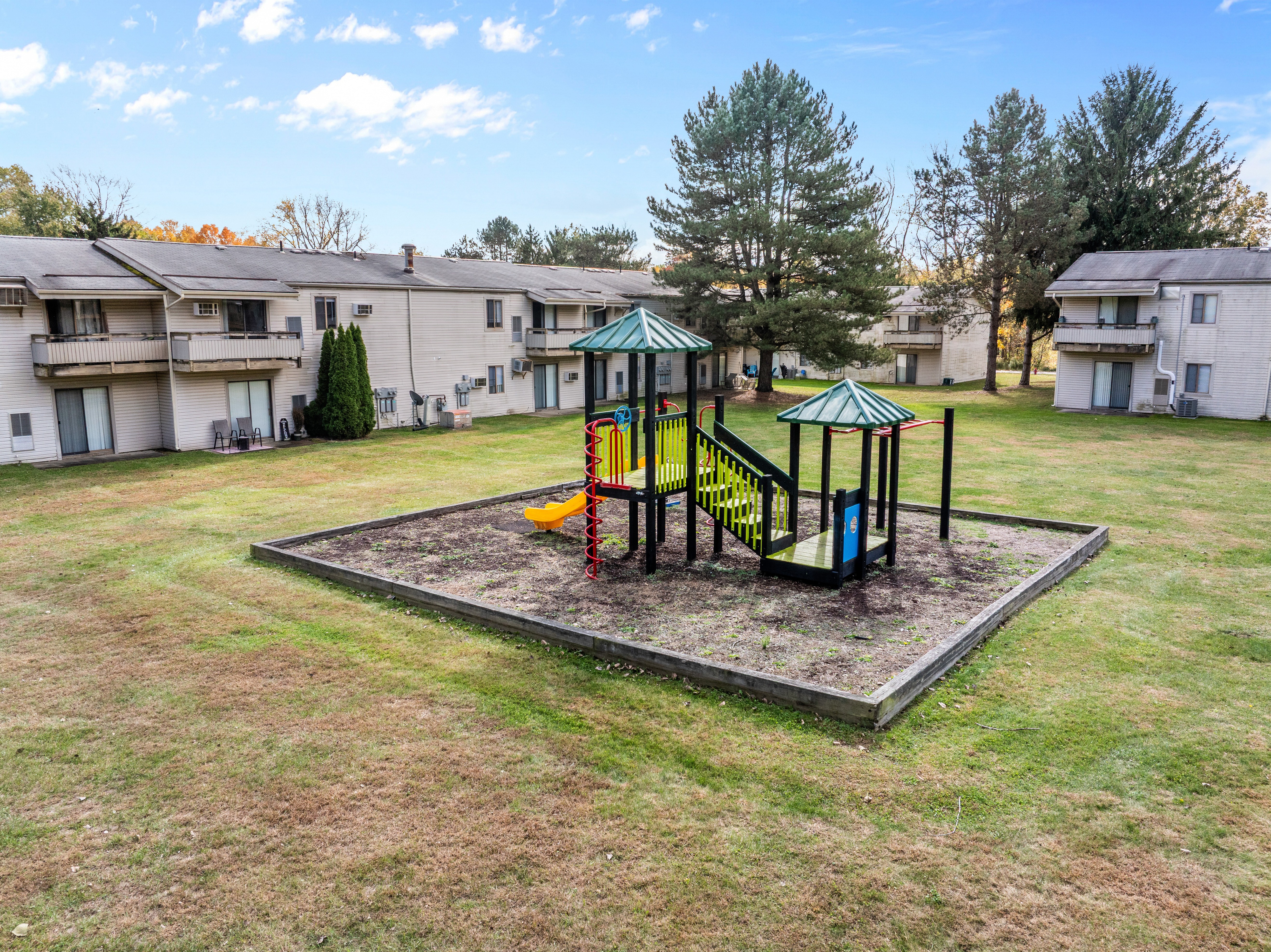 A playground with a yellow slide and a green roof is in the middle of a grassy area.